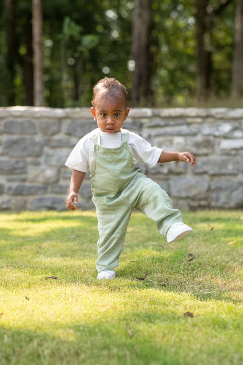 One year old black boy smiling and playing in grass at the park.